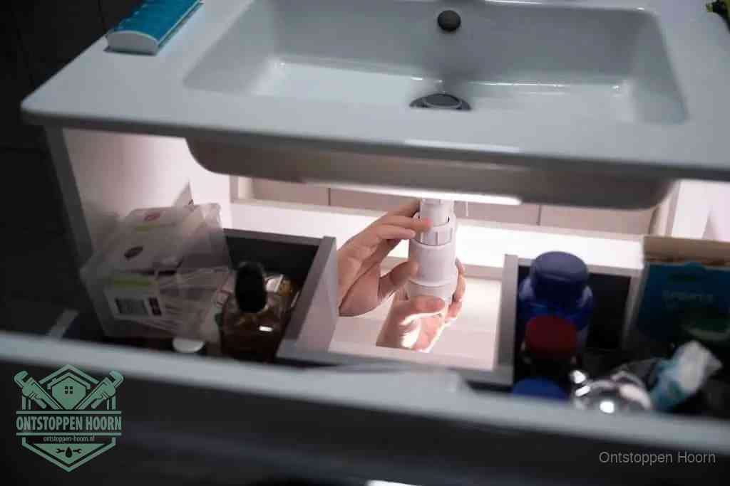 Een pompfles met zeep boven een wastafel, de heet water en afwasmiddel-methode om een vetprop in de afvoer los te maken in Hoorn