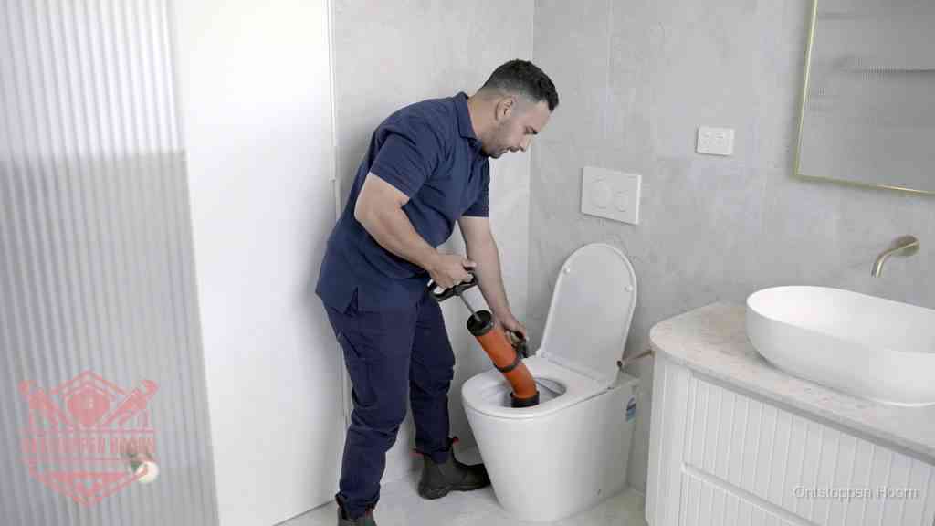 Een monteur buigt over een wandcloset en duwt met de hand een persluchtontstopper in de toiletpot om de verstopping handmatig los te maken in Hoorn
