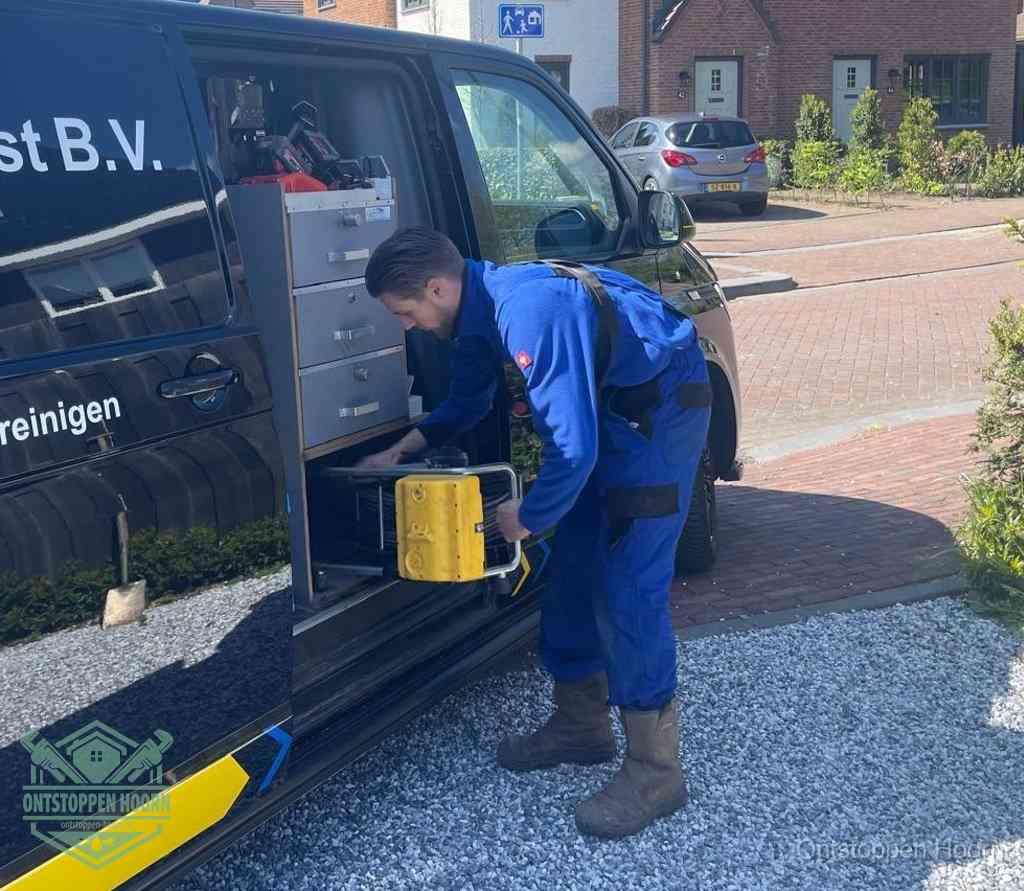 Een monteur pakt buiten op de oprit gereedschap uit de bedrijfsbus, het moment om een professional in te schakelen voor een verstopte afvoer in Hoorn