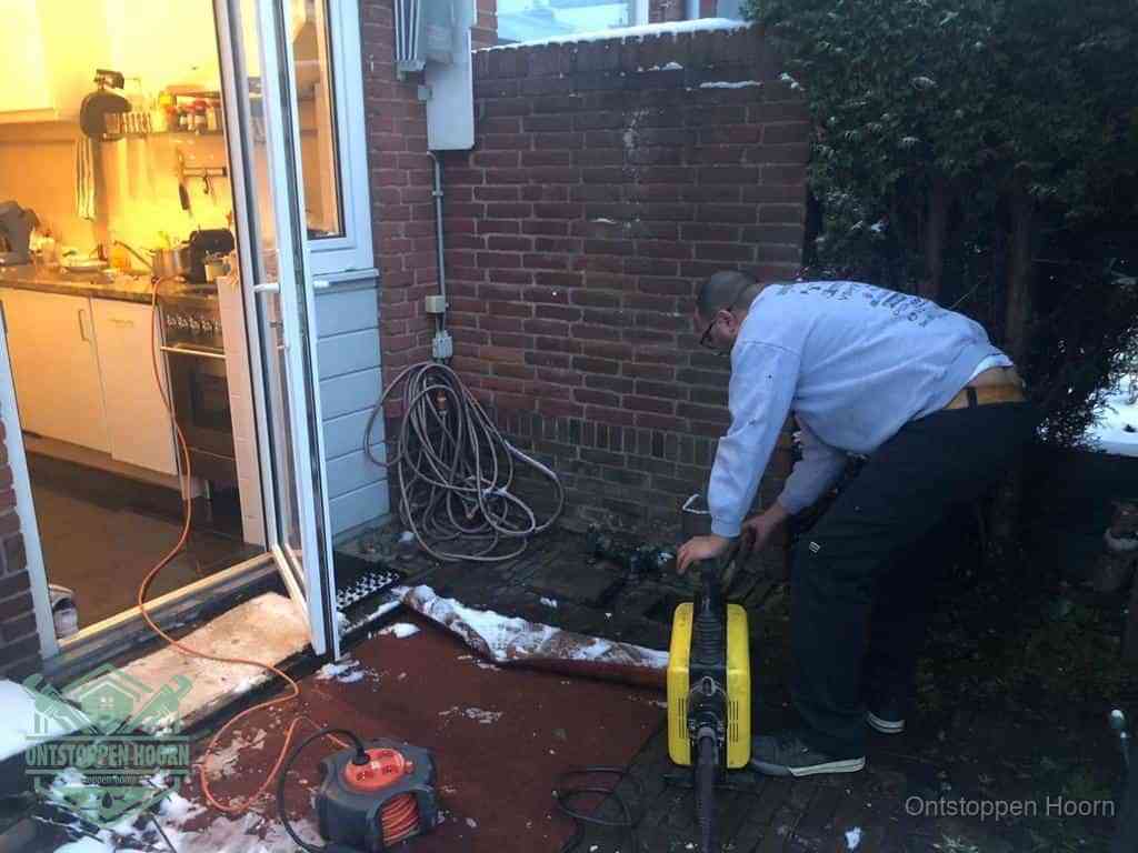 Een monteur werkt buiten bij een open riool-/grondput met een elektrische ontstoppingsmachine om een verborgen afvoerprobleem op te sporen in Hoorn