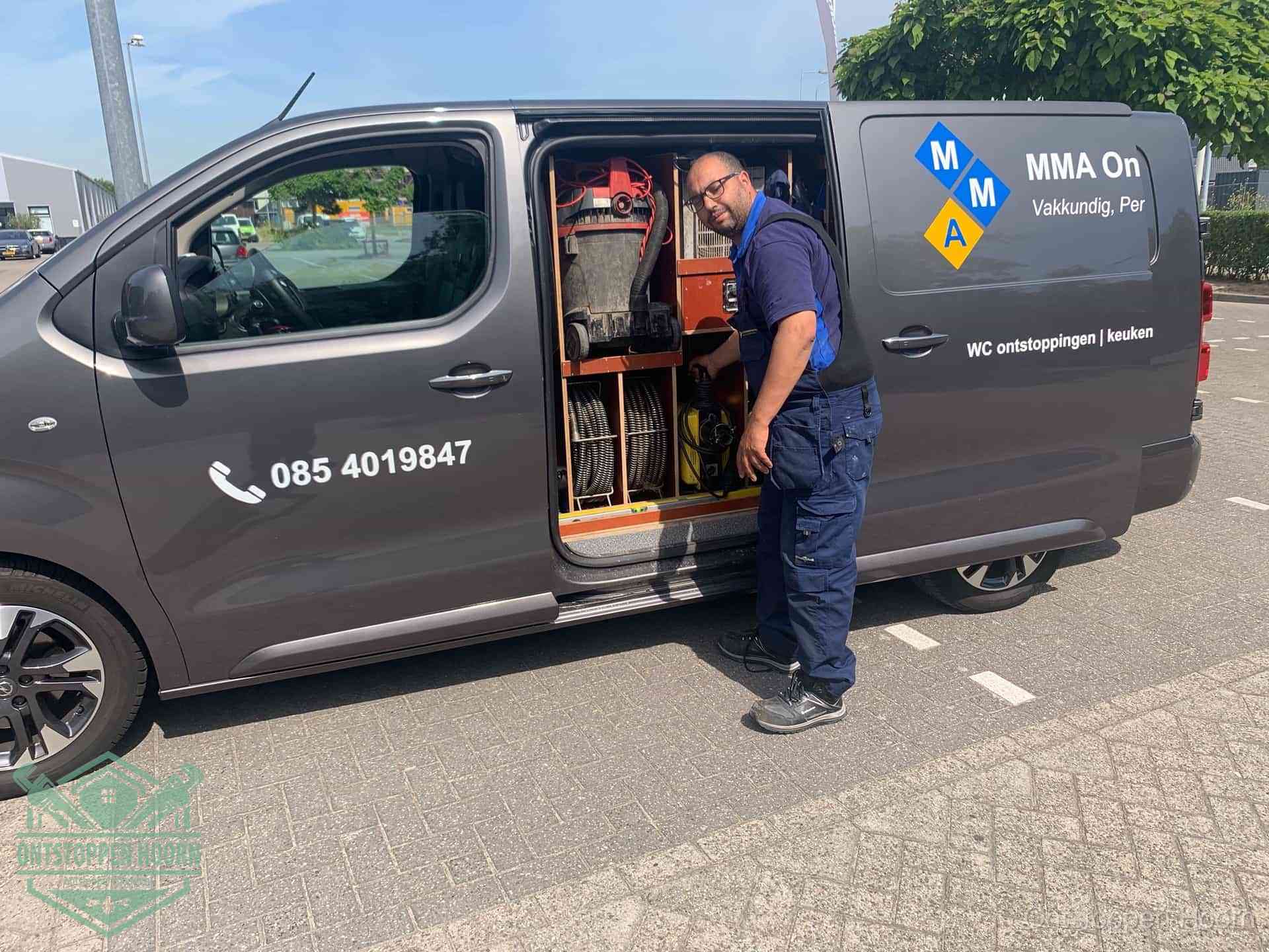 Een monteur bij de open schuifdeur van zijn bedrijfsbus op een parkeerplaats, klaar om de oorzaak van terugkerende afvoerverstoppingen aan te pakken in Hoorn