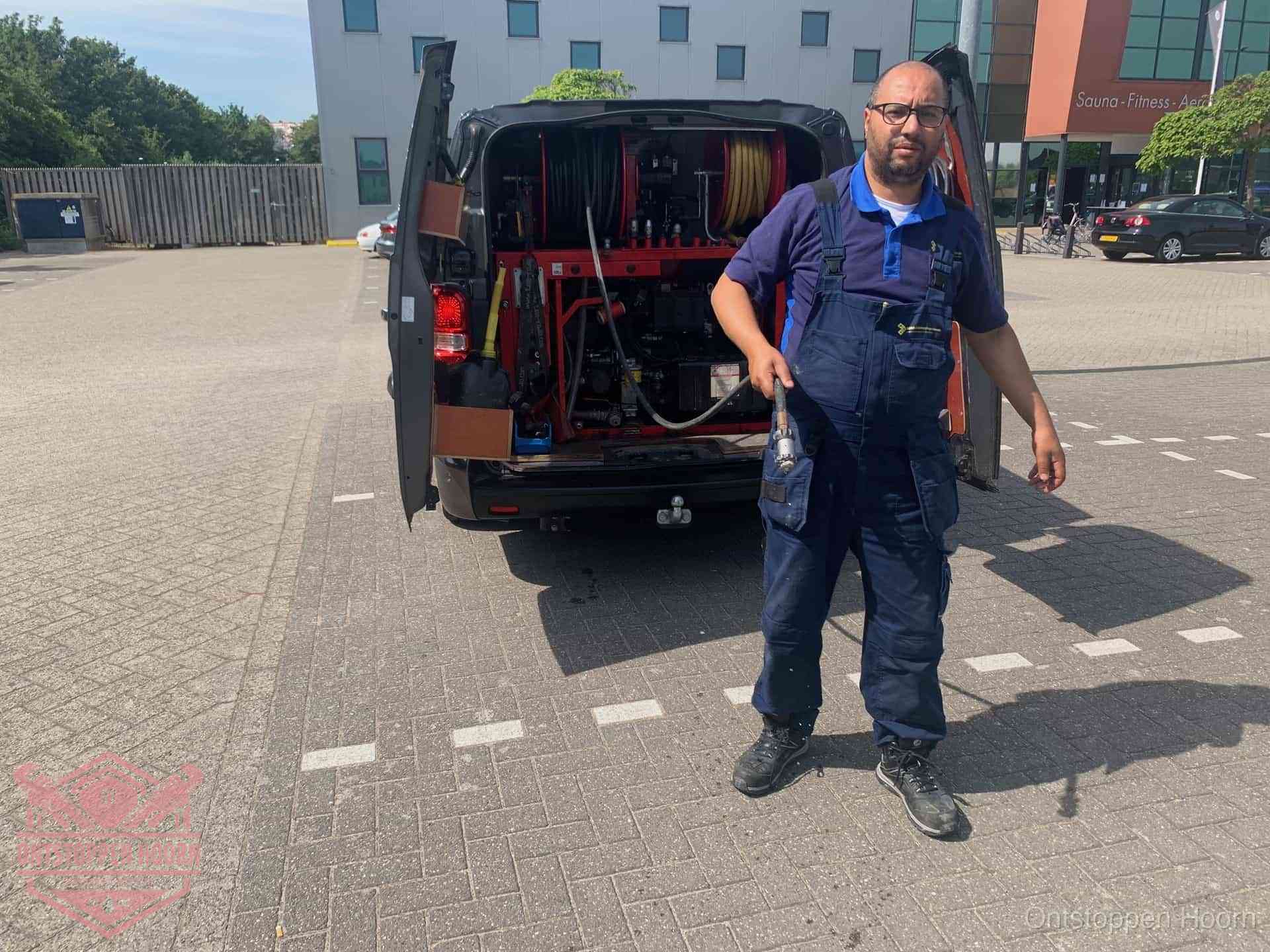 Een monteur bij zijn bestelbus met een hogedruk- en rioolreinigingsunit, klaar om de oorzaak van terugkerende wc-verstoppingen aan te pakken in Hoorn