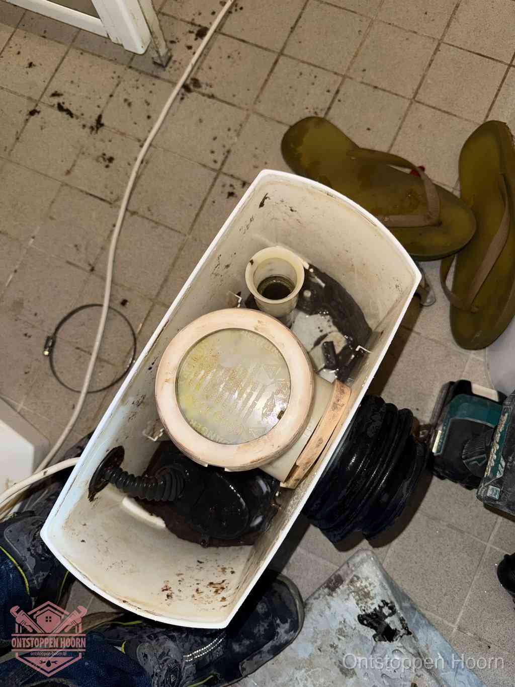 Een gedemonteerde toiletpot op de vloer met ontstoppingsveer en gereedschap ernaast, het verwijderen van een vastzittend voorwerp uit de wc in Hoorn