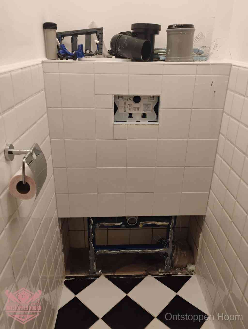 Een toiletruimte waar het hangtoilet en de inbouwreservoir-onderdelen zijn vrijgelegd voor onderhoud, periodiek nazicht voorkomt een wc-verstopping in Hoorn