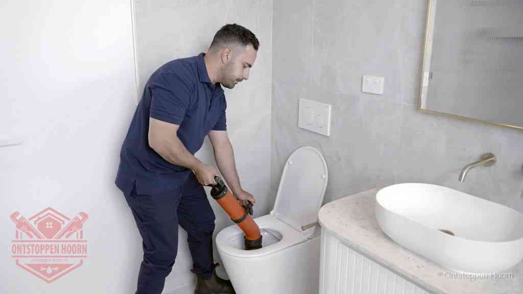 Een man gebruikt een handmatige luchtdruk-ontstopper in een modern betegeld toilet om zelf de wc te ontstoppen in Hoorn